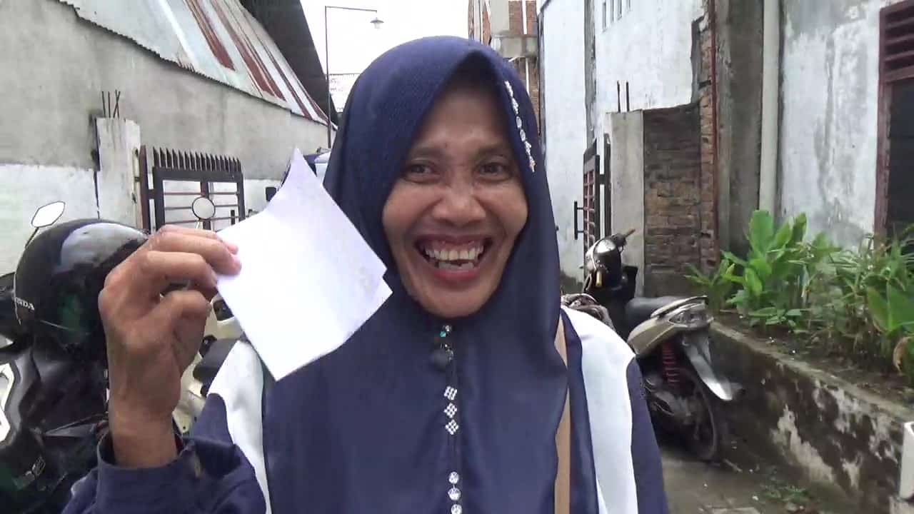 Sulia, warga Marelan, menunjukkan bingkisan dan amplop yang diterimanya usai menghadiri Sosperda Roma Uli Silalahi. Ia mengaku senang mendapatkan informasi seputar perumahan kumuh serta menerima bingkisan berupa botol sirup dan amplop berisi uang, Minggu, 23 Maret 2025, Zeze Futsal, Jalan Marelan Raya, Gang Sepakat, Kelurahan Rengas Pulau, Kecamatan Medan Marelan, Kota Medan (Foto: Dok. dahsyatnews.com).